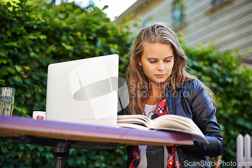 Image of Woman, book and laptop by cafe outdoors and sitting for reading, assignment or work. Young, female student and technology for online, submission or document for research, project or college test