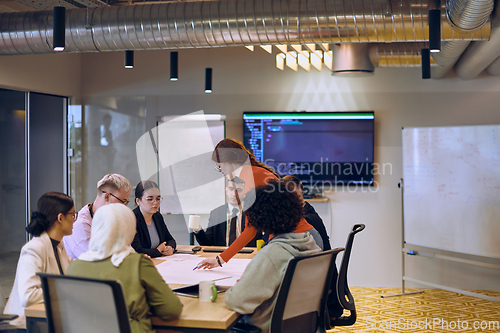 Image of A diverse team of business experts in a modern glass office, attentively listening to a colleague's presentation, fostering collaboration and innovation.