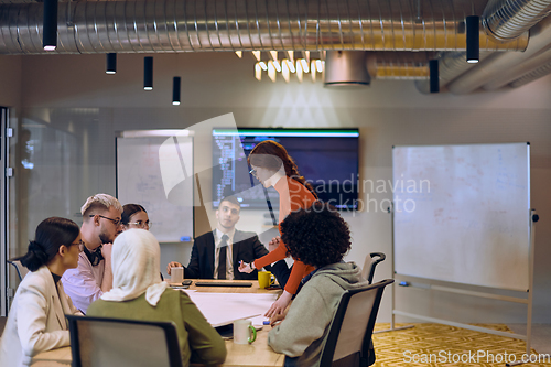 Image of A diverse team of business experts in a modern glass office, attentively listening to a colleague's presentation, fostering collaboration and innovation.