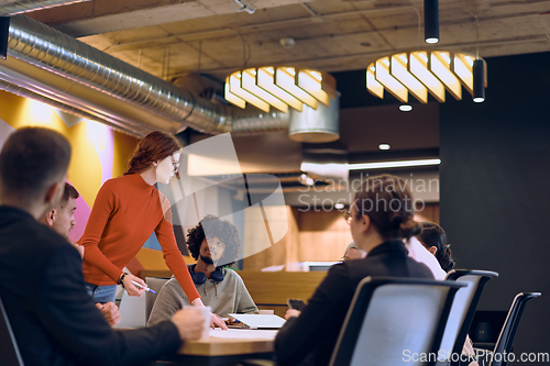 Image of A diverse team of business experts in a modern glass office, attentively listening to a colleague's presentation, fostering collaboration and innovation.