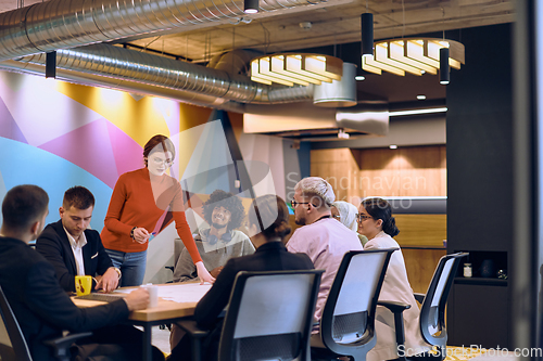 Image of A diverse team of business experts in a modern glass office, attentively listening to a colleague's presentation, fostering collaboration and innovation.