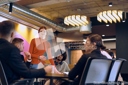 Image of A diverse team of business experts in a modern glass office, attentively listening to a colleague's presentation, fostering collaboration and innovation.