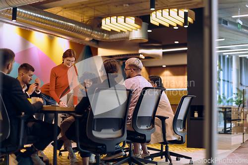 Image of A diverse team of business experts in a modern glass office, attentively listening to a colleague's presentation, fostering collaboration and innovation.