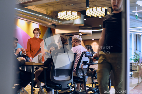 Image of A diverse team of business experts in a modern glass office, attentively listening to a colleague's presentation, fostering collaboration and innovation.