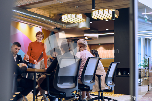 Image of A diverse team of business experts in a modern glass office, attentively listening to a colleague's presentation, fostering collaboration and innovation.