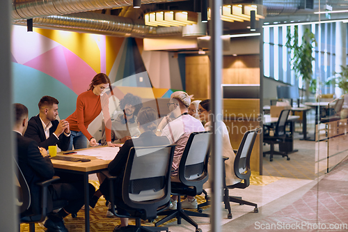 Image of A diverse team of business experts in a modern glass office, attentively listening to a colleague's presentation, fostering collaboration and innovation.