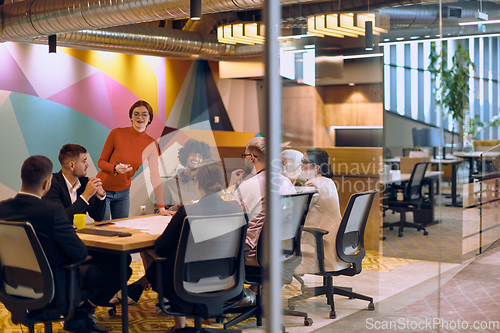 Image of A diverse team of business experts in a modern glass office, attentively listening to a colleague's presentation, fostering collaboration and innovation.