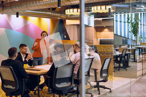 Image of A diverse team of business experts in a modern glass office, attentively listening to a colleague's presentation, fostering collaboration and innovation.