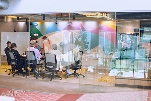 Image of A diverse team of business experts in a modern glass office, attentively listening to a colleague's presentation, fostering collaboration and innovation.