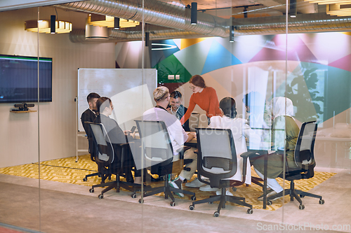 Image of A diverse team of business experts in a modern glass office, attentively listening to a colleague's presentation, fostering collaboration and innovation.