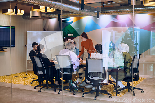 Image of A diverse team of business experts in a modern glass office, attentively listening to a colleague's presentation, fostering collaboration and innovation.