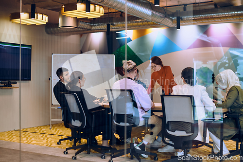 Image of A diverse team of business experts in a modern glass office, attentively listening to a colleague's presentation, fostering collaboration and innovation.