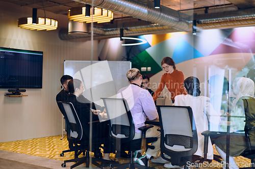 Image of A diverse team of business experts in a modern glass office, attentively listening to a colleague's presentation, fostering collaboration and innovation.