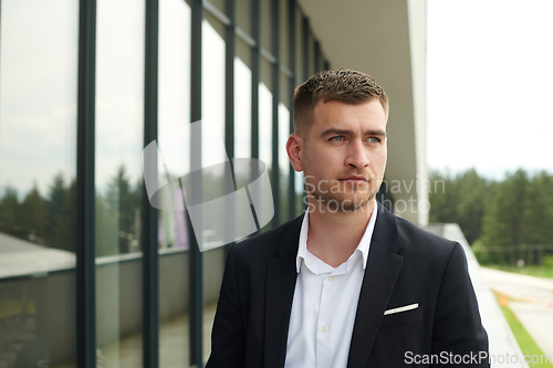 Image of A CEO dressed in a sleek black suit stands confidently at the entrance of a modern corporate building, awaiting the start of the workday in the bustling urban environment.