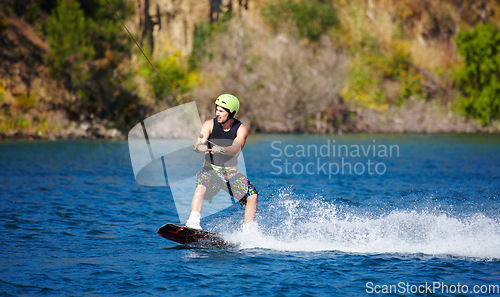 Image of Man, wakeboarding and water with helmet, sport and fitness for speed on vacation in summer sunshine. Person, athlete and ski with rope for safety on lake, sea or river for training, exercise or waves