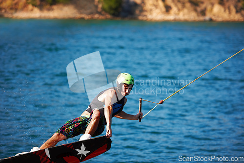 Image of Man, wakeboarding outdoor and lake with helmet, sport and fitness for speed in summer sunshine. Person, athlete and ski with rope for safety on water, sea or river for training, exercise and freedom