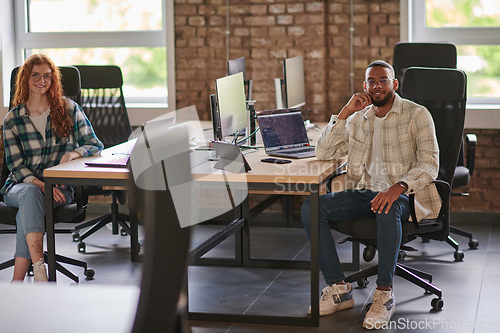 Image of Group of colleagues, a woman with vibrant orange hair and a young African American businessman, sitting in a modern office space, symbolizing diverse collaboration and a dynamic work environment.