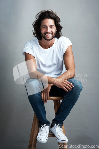 Image of Fashion, smile and portrait of man in studio on a stool with casual, cool and stylish outfit. Happy, handsome and confident young male model from Mexico with trendy style on chair by gray background.