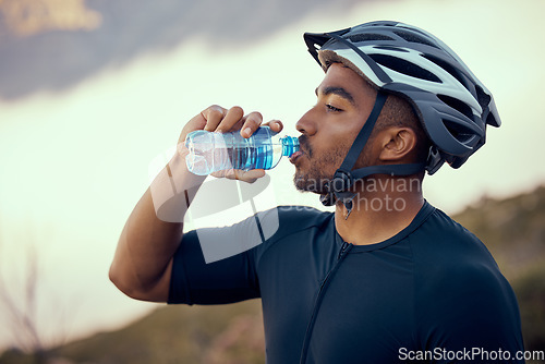 Image of Fitness man, cycling and drinking water bottle and wearing safety helmet outdoors in nature during summer. Male athlete, exercise and hydration riding a bike to practice, workout or train for sports