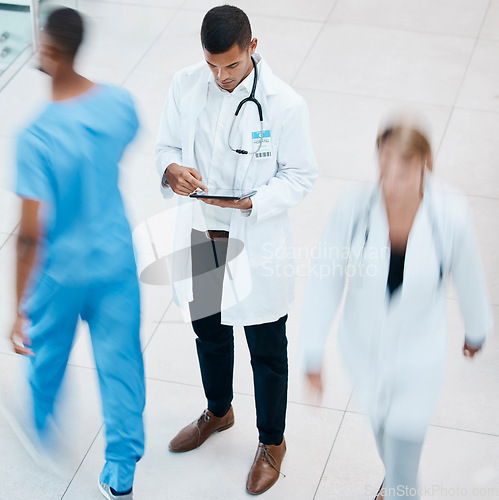 Image of Busy hospital with doctor browsing on tablet for test results, patient records and medical research from above. Healthcare professional and expert working on treatment plan in a bustling clinic