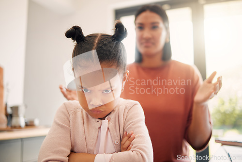 Image of Angry little girl, unhappy and upset after fight or being scolded by mother, frowning with attitude and arms crossed. Naughty child looking offended with stressed single parent in background.