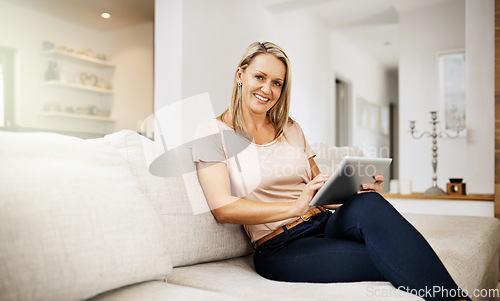 Image of Carefree and relaxed woman browsing on a tablet, enjoying her weekend and sitting on the sofa at home. Portrait of a mature comfortable, happy female surfing the internet in the living room