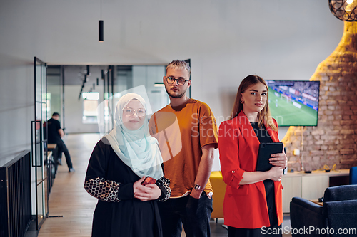 Image of A group of young business colleagues, including a woman in a hijab, stands united in the modern corridor of a spacious startup coworking center, representing diversity and collaborative spirit.