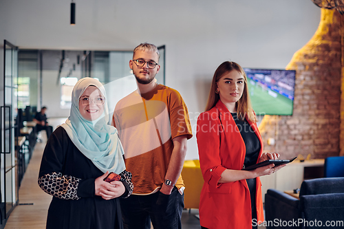 Image of A group of young business colleagues, including a woman in a hijab, stands united in the modern corridor of a spacious startup coworking center, representing diversity and collaborative spirit.