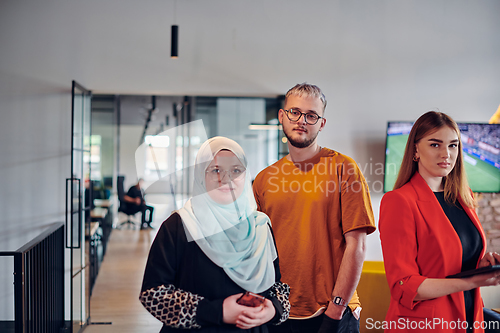 Image of A group of young business colleagues, including a woman in a hijab, stands united in the modern corridor of a spacious startup coworking center, representing diversity and collaborative spirit.