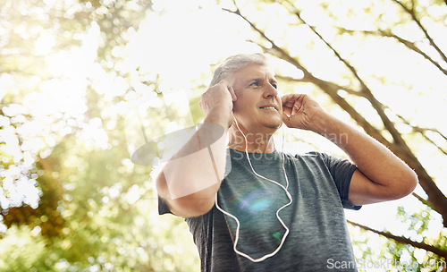 Image of Healthy, fit and active senior man listening to music while running, exercising and training outside from below. Happy, sporty and real mature male doing a cardio and endurance workout outdoors