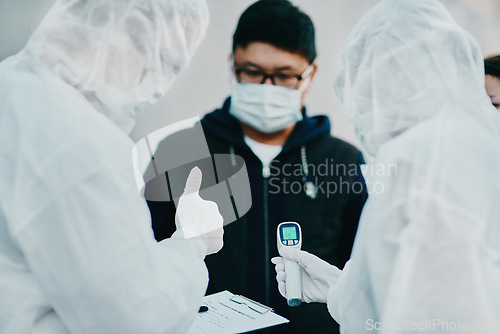 Image of Negative covid test and thumbs up for young man from healthcare worker after testing for virus. Medical professionals in hazmat suits taking temperature tests during disease outbreak or pandemic
