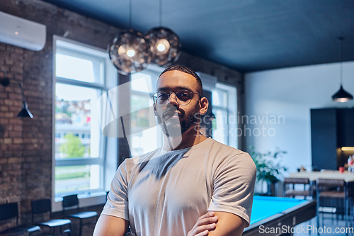 Image of An African American businessman posing with crossed arms, exuding confidence and empowerment within the modern business setting of a startup coworking center.