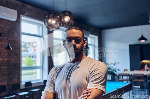 Image of An African American businessman posing with crossed arms, exuding confidence and empowerment within the modern business setting of a startup coworking center.