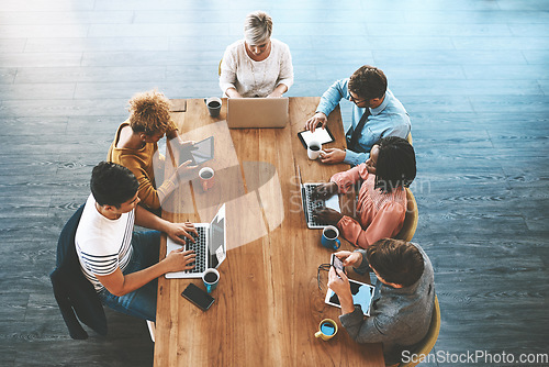 Image of Innovation, digital marketing and planning online with laptop and tablet while creative team sit together at a table from above. Group of designers doing research or building social media network