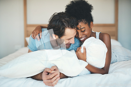 Image of Fun interracial couple laughing, bonding and lying on bed in a home bedroom and looking happy, in love and playful. Smiling man and woman hugging and cuddling after waking up in the morning together