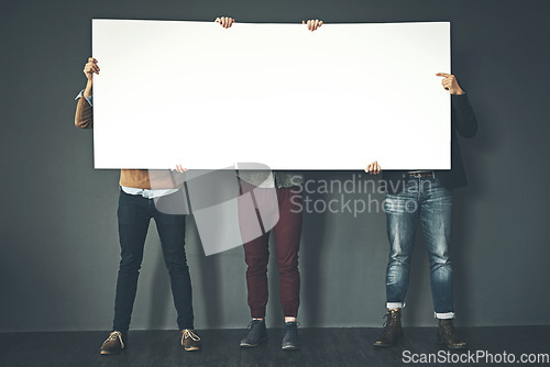 Image of Group of businesspeople holding up a copyspace sign voicing their opinion at work with a grey background. People with blank poster advertising, marketing and express or convey important messages