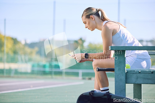 Image of Fit tennis player with phone checking fitness goal progress on a sports exercise app online while taking a break at the court. A sportswoman checking messages on cellphone and waiting for a coach