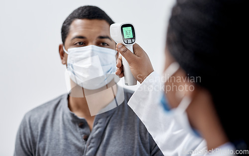 Image of Male covid patient getting his temperature taken with medical equipment by a doctor in hospital consultation room. Man wearing mask and health care professional pointing digital infrared thermometer.