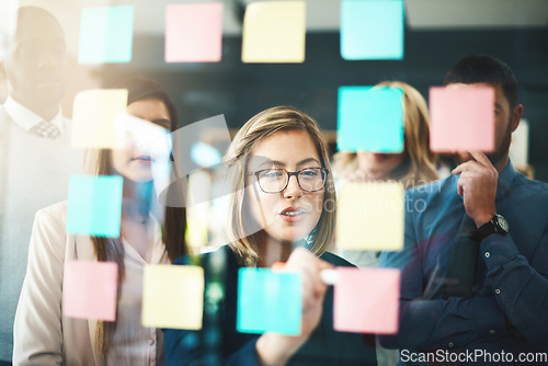 Image of Talking team leader writing on sticky notes while planning, innovating or sharing business vision or ideas. Diverse group of motivated, ambitious or learning creative business people meeting together