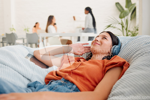 Image of Relaxing, carefree and listening to music with a young business woman thinking, resting and lying in an office during break. Enjoying the comfort of a beanbag chair and working as a creative designer