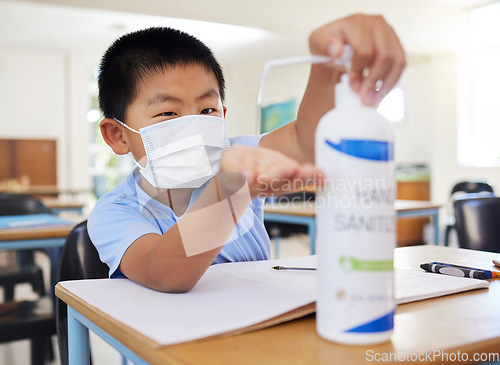 Image of Hygiene, safety and covid routine of a little boy using hand sanitizer at school. Young asian student with a mask practicing good health by cleaning his hands at his classroom desk in a pandemic