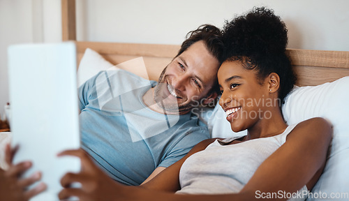 Image of Happy, relax and carefree interracial couple on digital tablet smiling and taking a selfie in bed. Husband and wife waking up and reading social media news on touchscreen while relaxing at home.