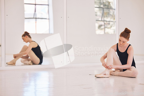 Image of Female ballet dancer preparing pointe shoes in a ballet hub, studio or class with mirror reflection of her sitting on the floor. Young, single ballerina performer getting ready for practice rehearsal