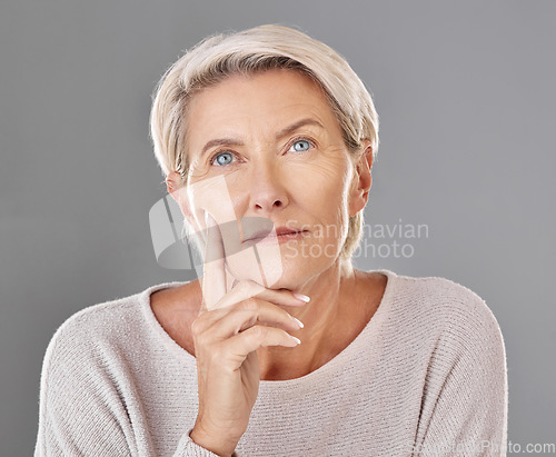 Image of Mature, thinking and woman touching her face in isolated grey studio background. Copy space for anti ageing skincare or cosmetic products for senior feeling her skin and wrinkles headshot.
