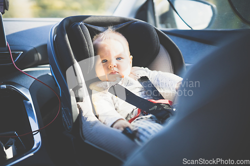 Image of Cute little baby boy strapped into infant car seat in passenger compartment during car drive.