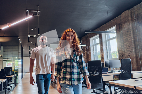 Image of A woman with modern orange hair and an African American businessman walking together through the hallway of a contemporary coworking startup office, reflecting diversity and collaboration