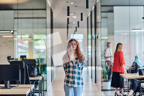 Image of A portrait of a young businesswoman with modern orange hair captures her poised presence in a hallway of a contemporary startup coworking center, embodying individuality and professional confidence.