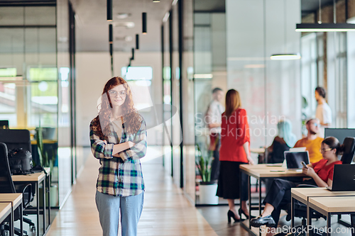 Image of A portrait of a young businesswoman with modern orange hair captures her poised presence in a hallway of a contemporary startup coworking center, embodying individuality and professional confidence.