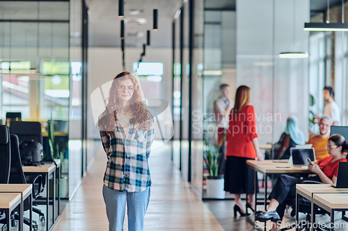 Image of A portrait of a young businesswoman with modern orange hair captures her poised presence in a hallway of a contemporary startup coworking center, embodying individuality and professional confidence.