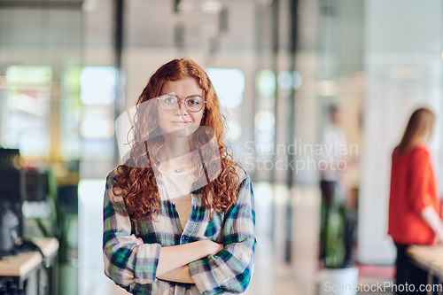 Image of A portrait of a young businesswoman with modern orange hair captures her poised presence in a hallway of a contemporary startup coworking center, embodying individuality and professional confidence.